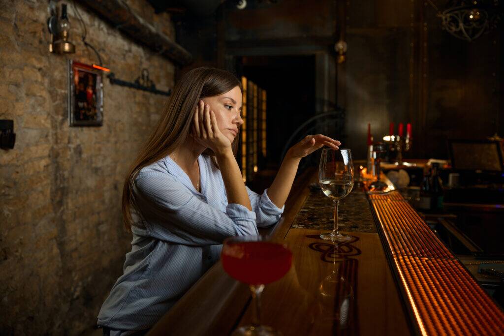 Lonely sad woman sitting at bar feeling depressed and unhappy. Problem with alcoholism and alcohol abuse